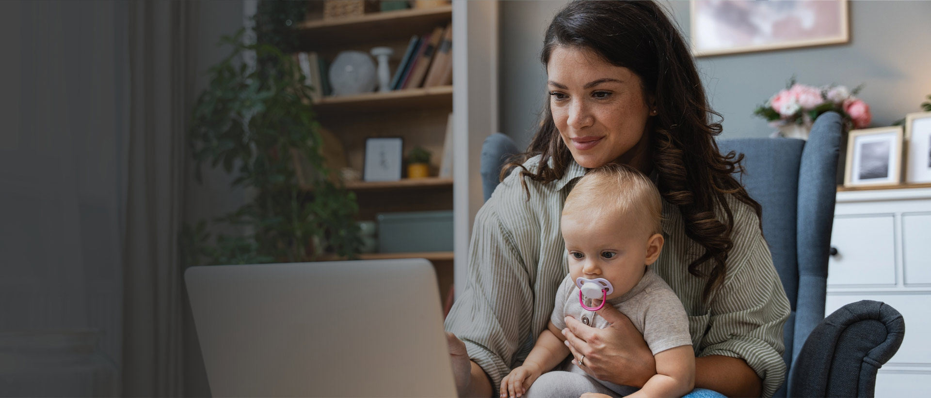 Mother holding baby while looking at laptop