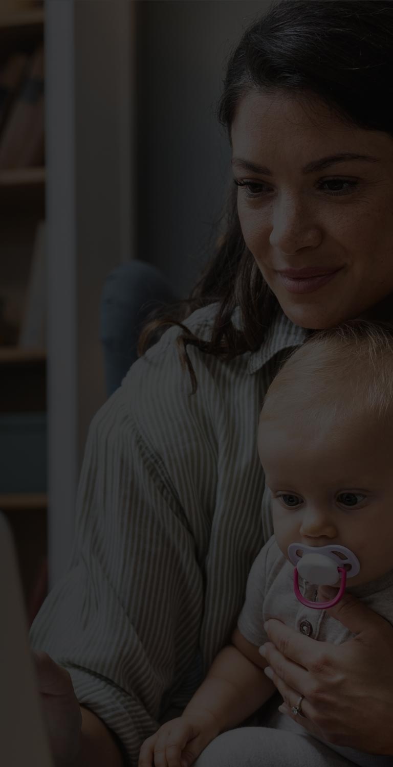 Mother holding baby while looking at laptop mobile